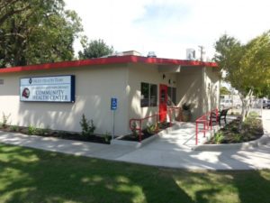 Entrance to the Kerman School-Based Health Center with an accessible ramp and red railings leading to the red front door.