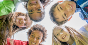 Five pre-teen children form a circle while looking down and smiling.