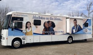 A mobile van is parked in a lot with a large photo of children and teens and the words Medicine on the Move.